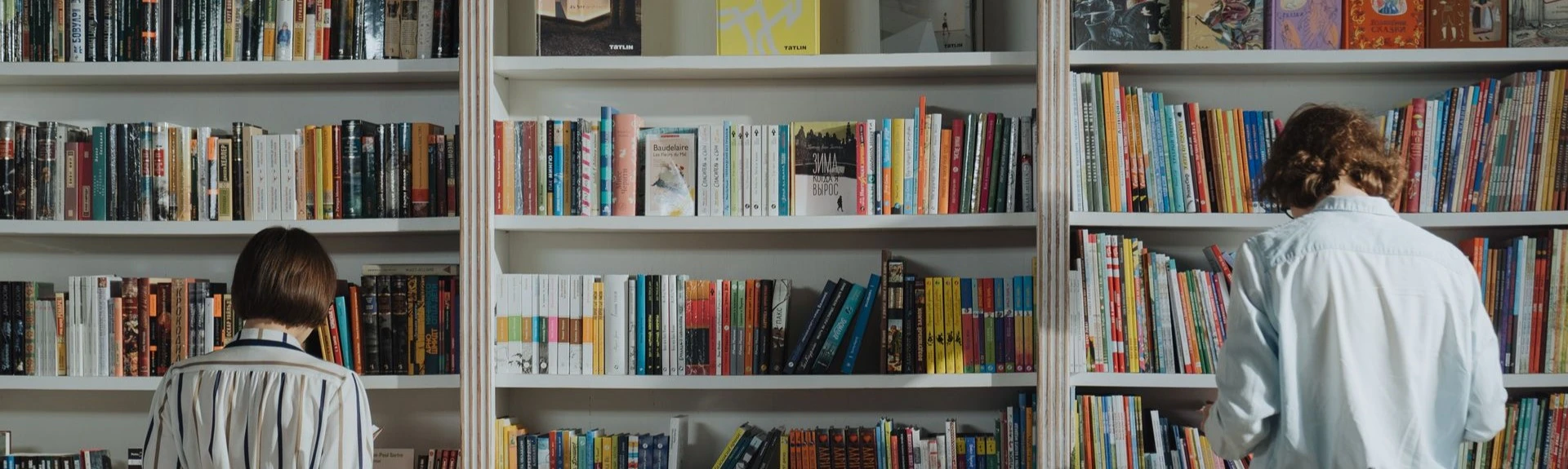 Twee personen bekijken boeken in een bibliotheek op zoek naar nieuwe inzichten voor persoonlijke en professionele groei.